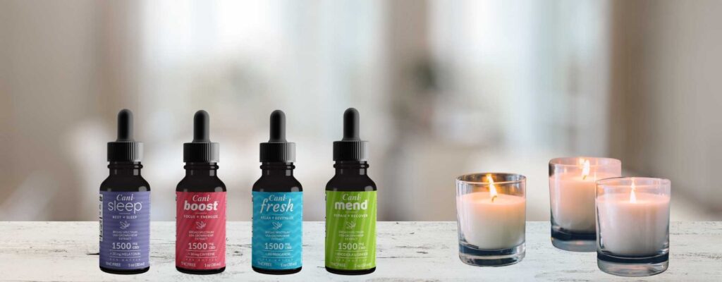 Four CBD oil tinctures next to three lit candles on a marble table