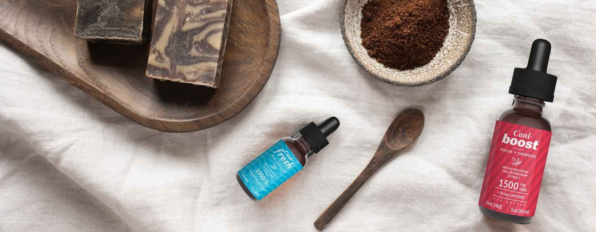 Alt=“CBD oil tincture for relaxation and CBD oil tincture with energy boost next to spoon, coffee powder and soap bars”