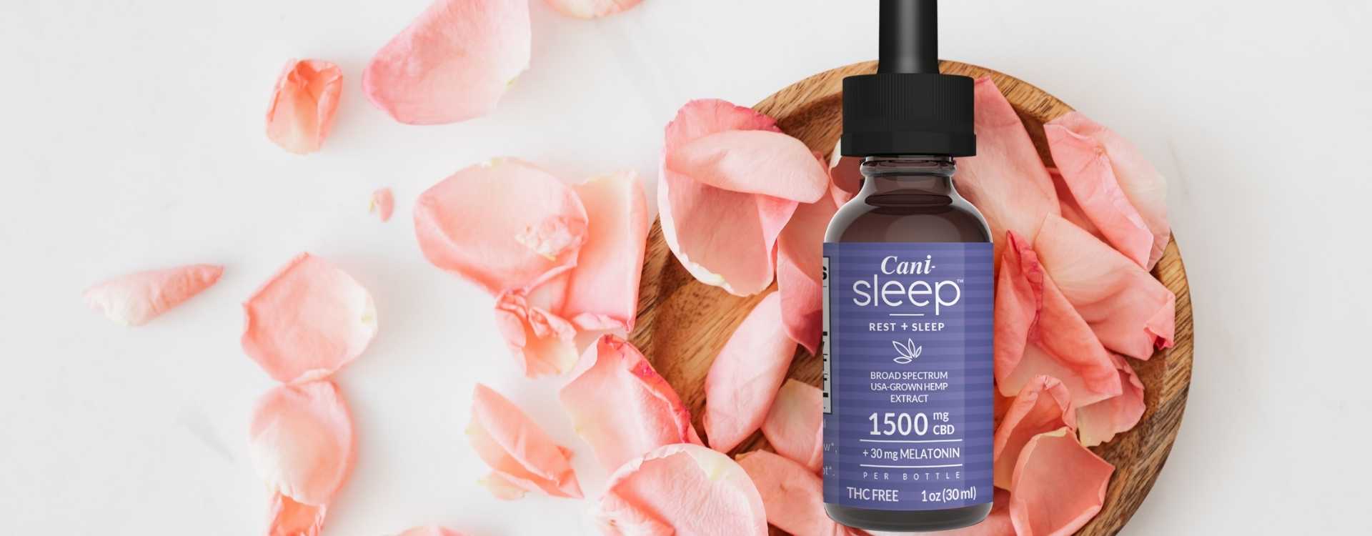 Alt=“CBD oil tincture for sleep placed on a wooden bowl surrounded by pink flower petals”