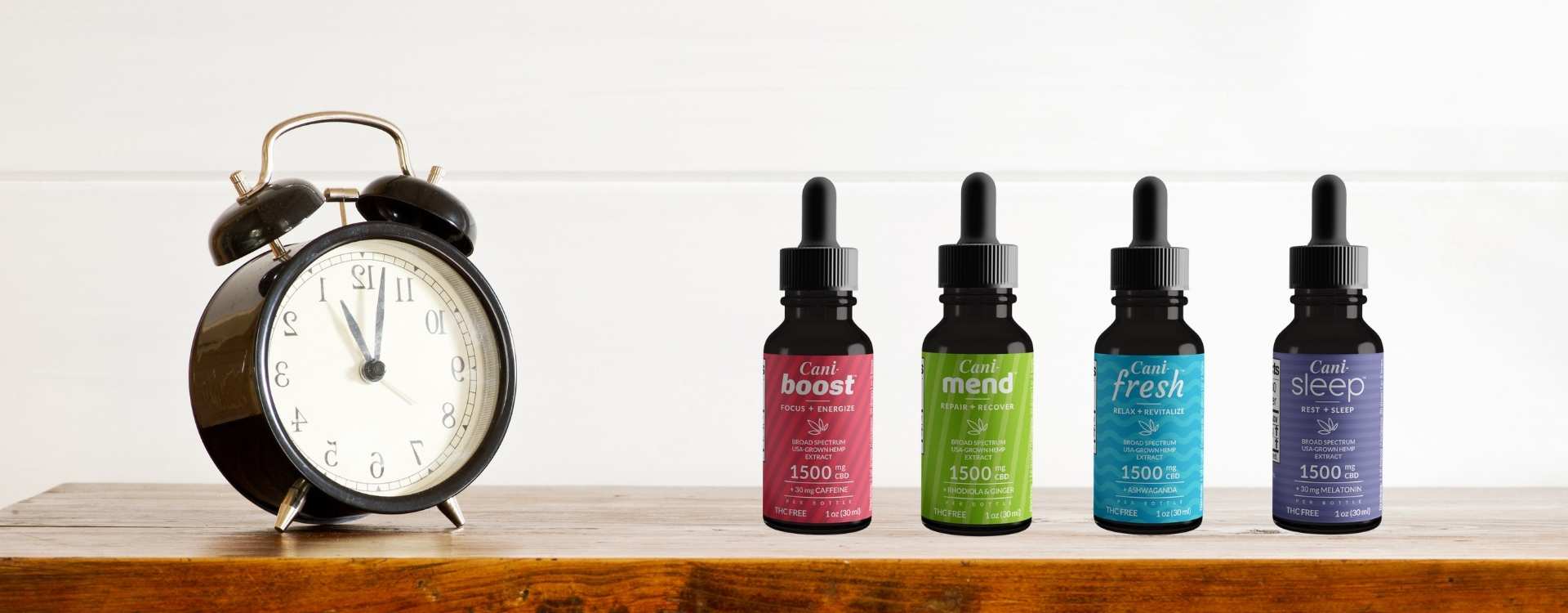 A black clock next to four oil tinctures on a wooden bedside table
